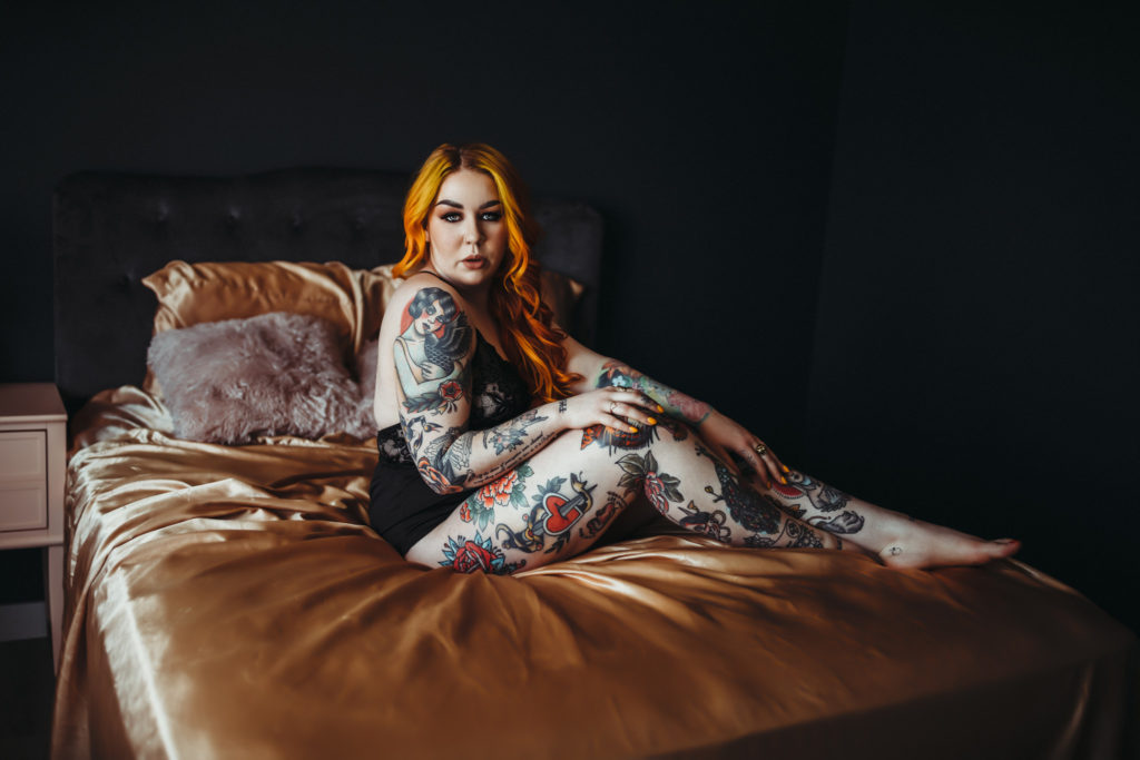 tattoed woman with orange hair on gold sheets